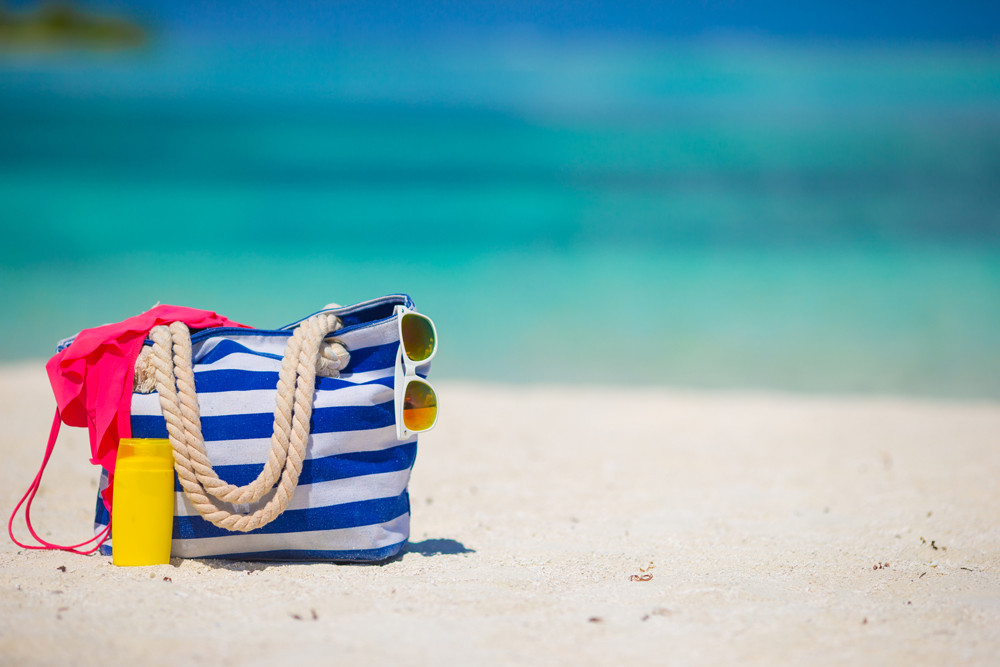 Blue bag, straw hat, flip flops and towel on white beach